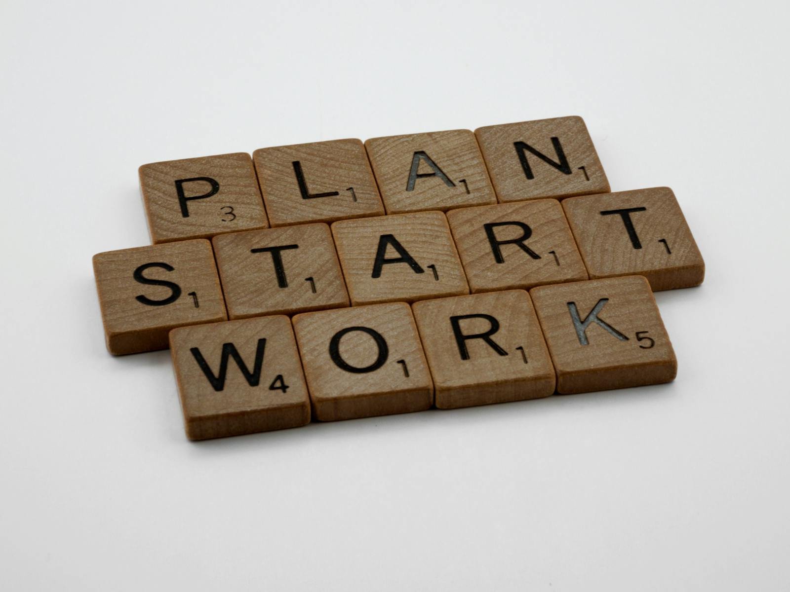 Wooden Scrabble tiles spelling 'Plan', 'Start', 'Work' on a white background.